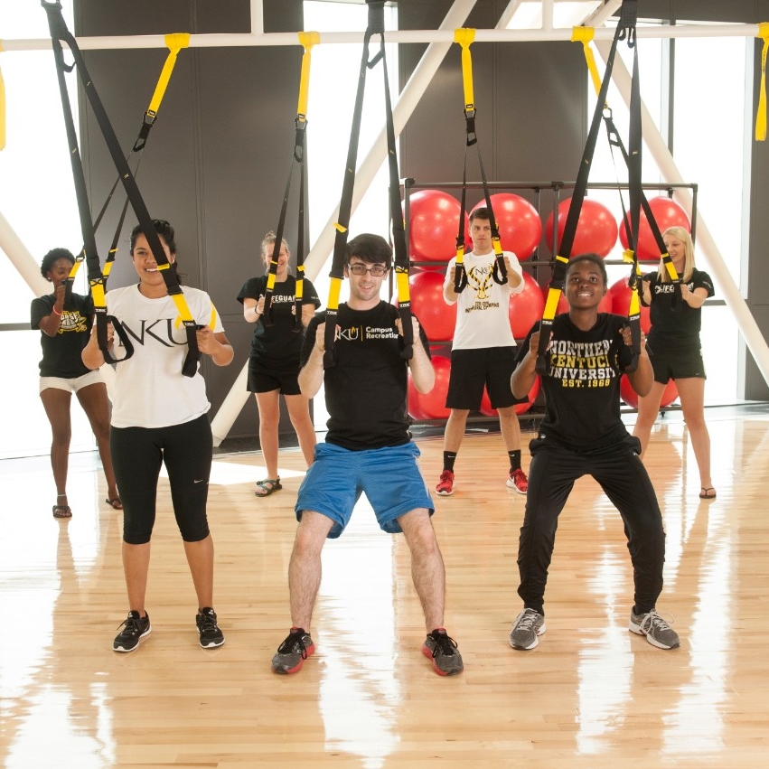 Seven students participating in a fitness class inside a campus rec gym.