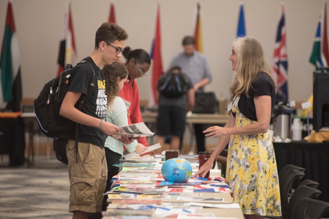 A student looks at a table of flyers for study abroad programs in a room of with flags from different countries. 